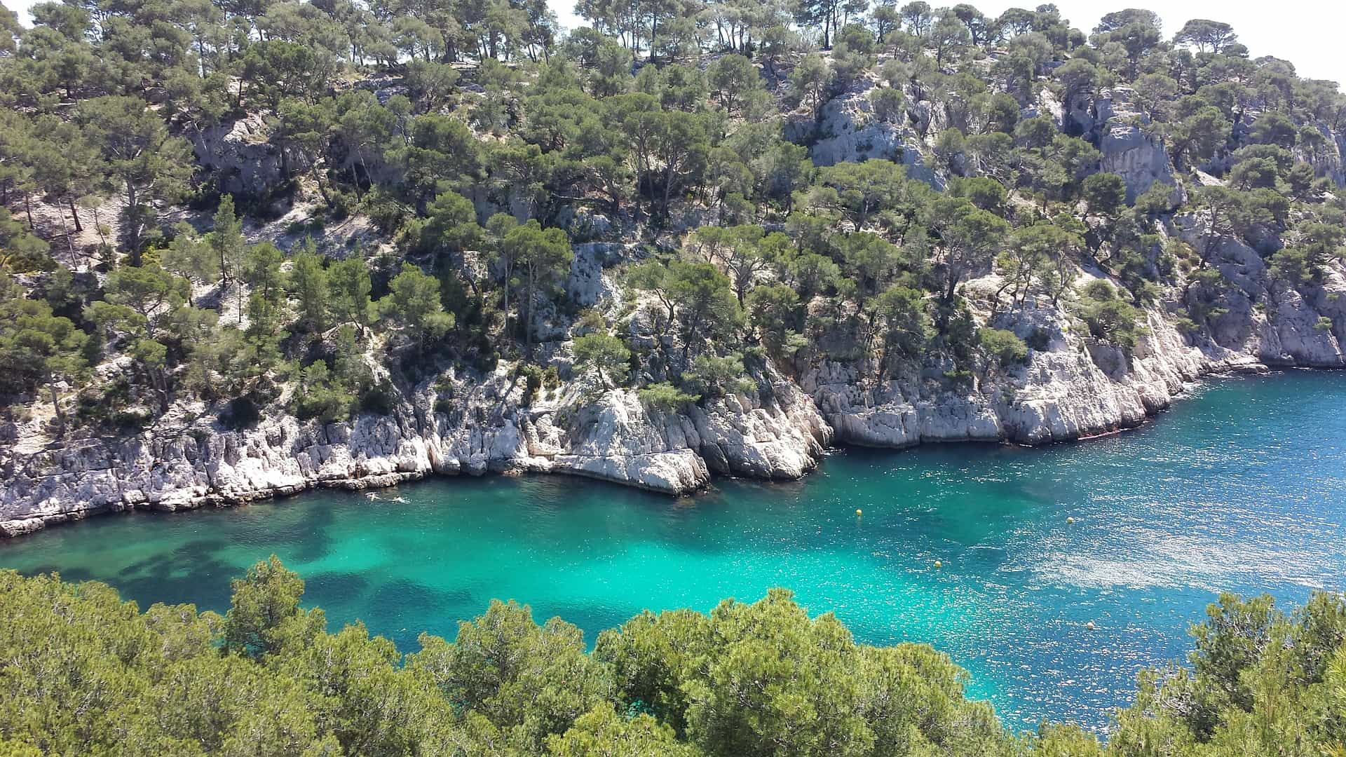 Hikers on a trail along limestone cliffs with a view of the Mediterranean sea in the background